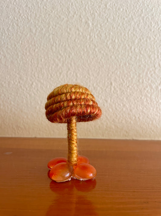 Golden mushroom collectible Made with golden orange and yellow yarn wrapped around rope and shaped into a mushroom with small flat platform adorned with glass beads for standing, perfect for mushroom lovers and or collectors, can also be used as an ornament (hook is included in order)  Materials: yarn, rope, glass beads, hot glue