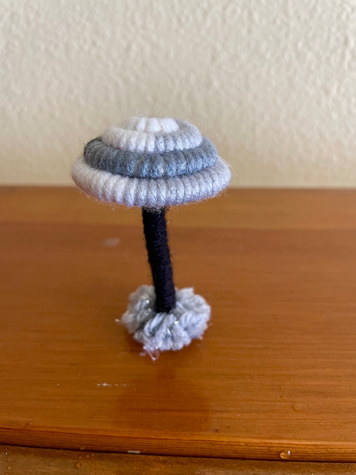 Made with gray black and white yarn wrapped around rope and shaped into a mushroom with small flat platform for standing, perfect for mushroom lovers and or collectors, can also be used as an ornament (hook is included in order)