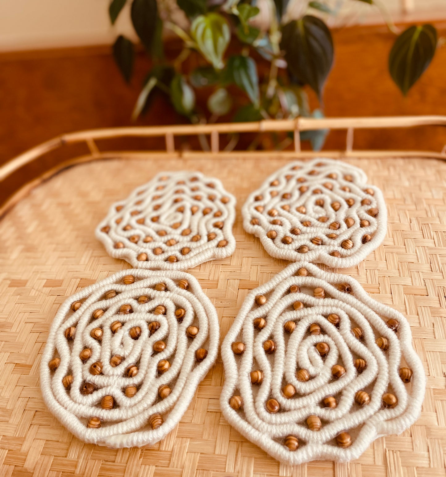 Very unique coaster set made with cream yarn wrapped rope with brown wood beads embedded throughout for a lattice pattern.  Materials: acrylic yarn, rope, wood beads, hot glue, felt fabric (on bottom)