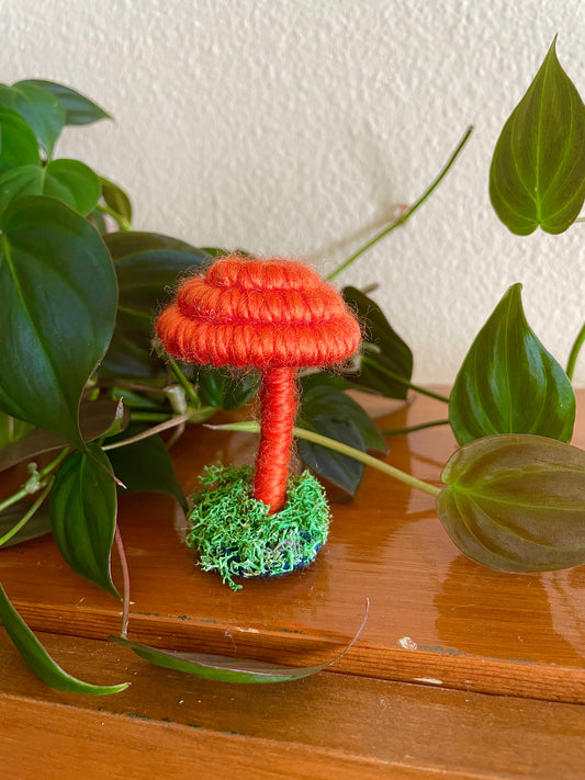 Orange mushroom collectible Made with orange yarn wrapped around rope and shaped into a mushroom with small flat platform adorned with moss for standing, perfect for mushroom lovers and or collectors, can also be used as an ornament (hook is included in order)  Materials: acrylic yarn, rope, hot glue  Dimensions: