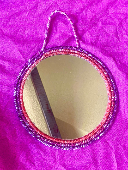 Ombre Orange white and purple hues yarn wrapped around rope on the frame on an 8 inch mirror with strap for hanging  Dimensions: 12.5x9.5 inches  Materials: 8 inch round mirror, yarn, felt fabric