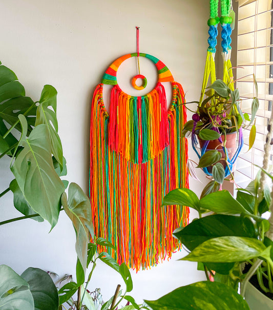 Beautiful mix of bright colors in orange yellow and green tones, has wrapped detail on top with circle ring in the upper top center, with 2 layers of fringe and gold tube bead detail.  Materials: yarn, bamboo hoops, wood ring, gold tube beads  Dimensions:33 inches L x12.5 W