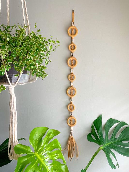 raffia and shells garland Vertical garland made with raffia wrapped around wood circles and embellished with shells on raffia braid with tassel on the bottom  Dimensions: 34 inches long, 2 inches wide  Materials: Raffia, wood circles, shells, hot glue   